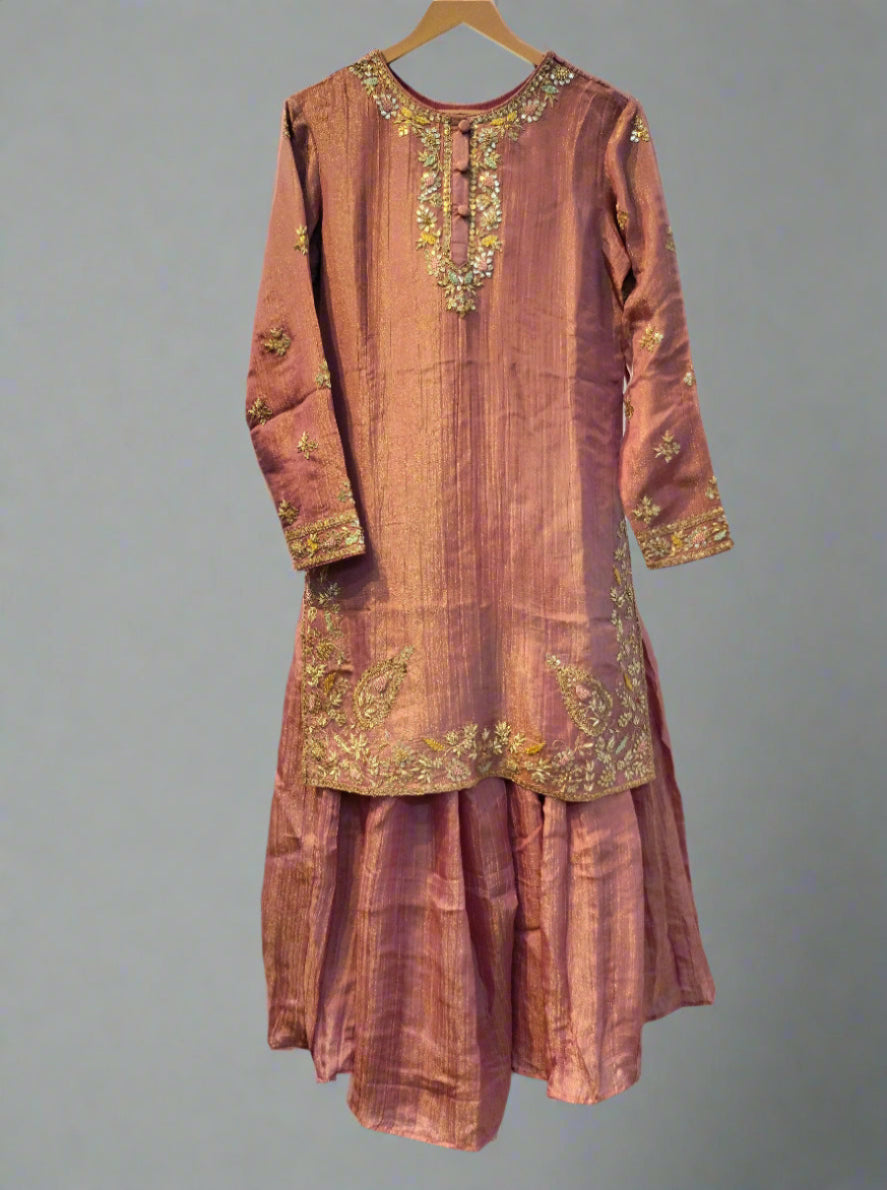 Pink traditional outfit with gold embroidery on a hanger against a neutral background