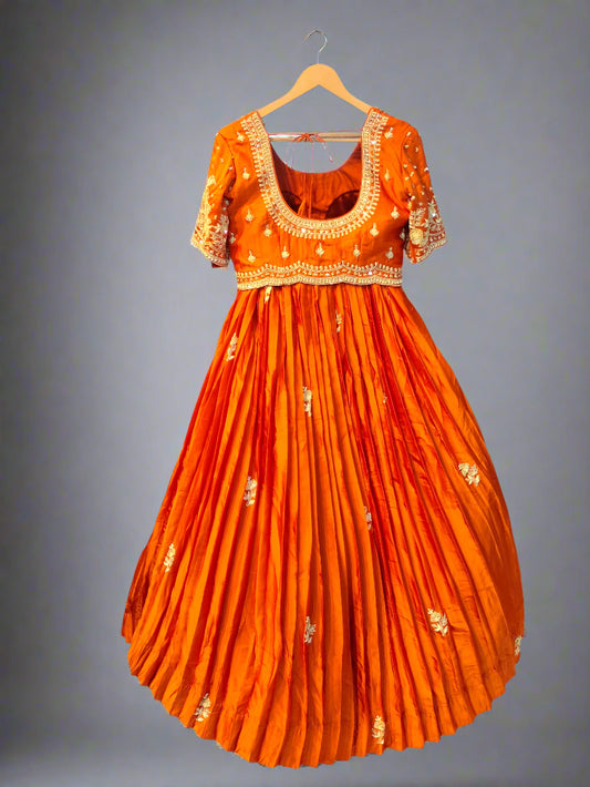 Orange dress with gold embroidery on a hanger against a metallic background