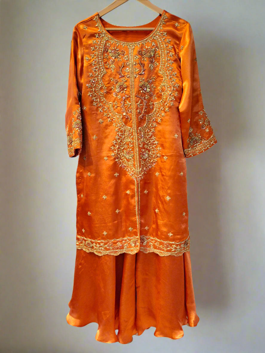 Orange embroidered dress on a hanger against a neutral background